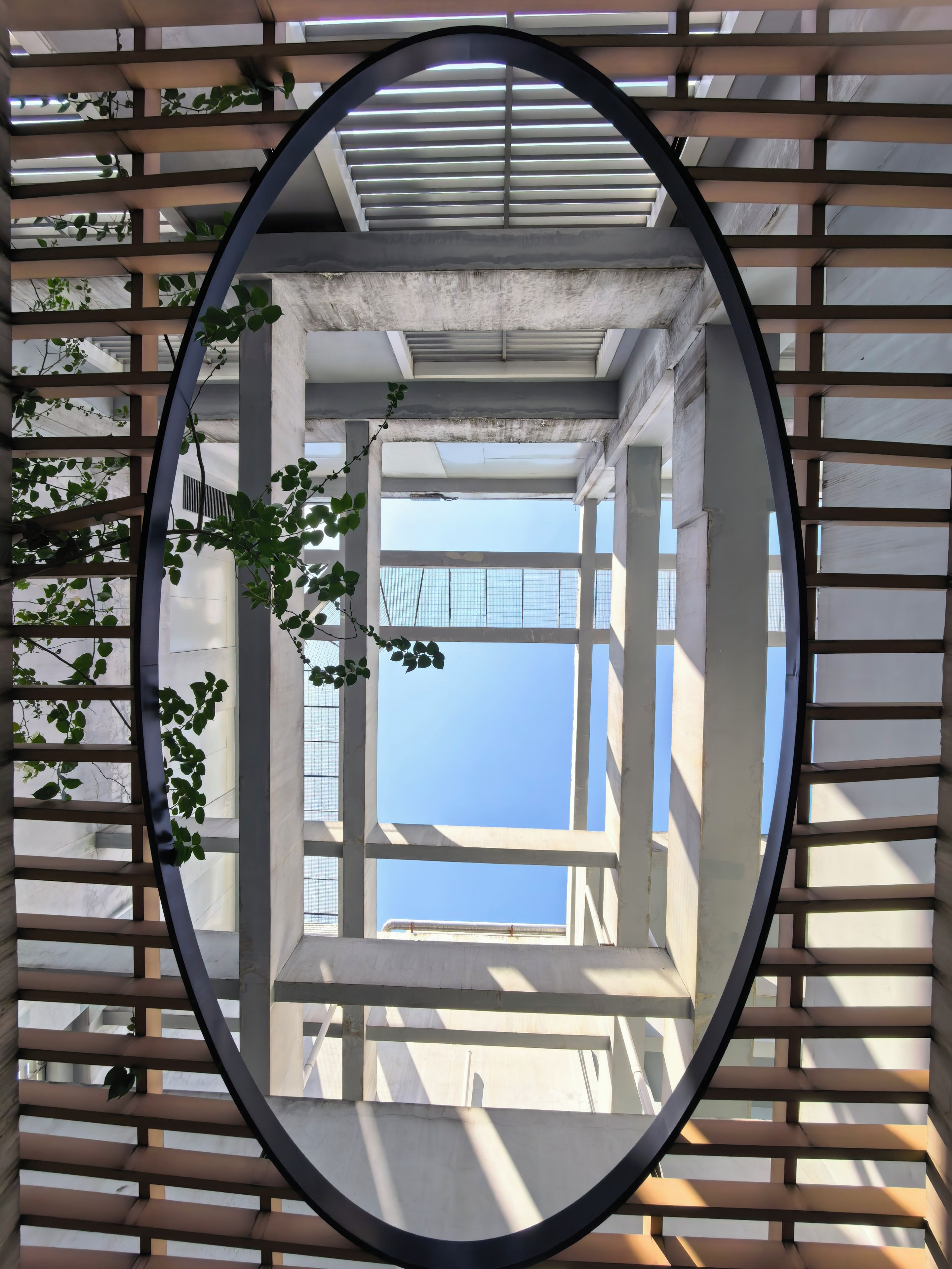 Un espejo circular refleja un interior moderno con techo de hormigón y vistas al cielo.