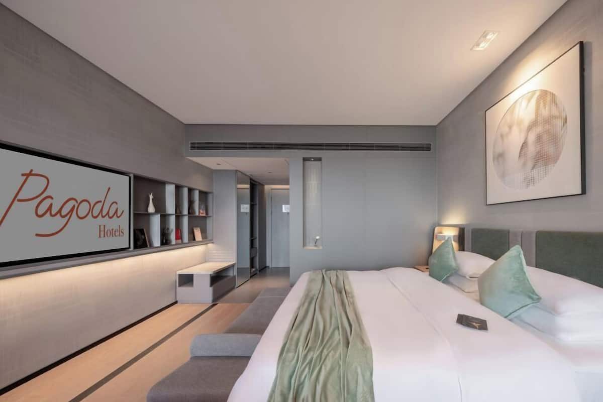 A modern hotel room with a large bed, bedside tables, a wall-mounted TV, and a framed artwork.