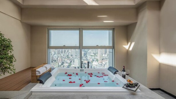 Un spa moderno con una bañera grande, vistas a la ciudad y una pequeña mesa con una botella y vasos.