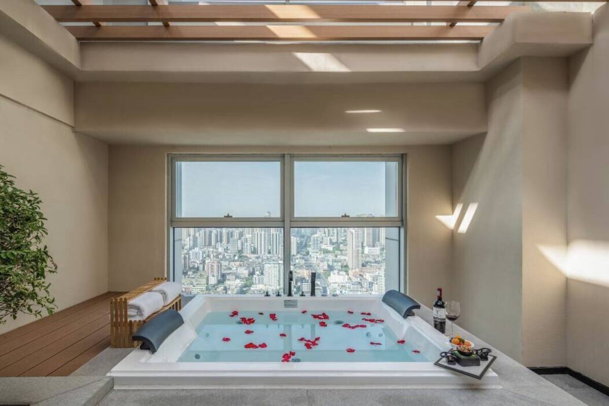 A modern spa room with a large bathtub, a city view, and a small table with a bottle and glasses.
