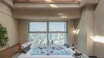 A modern spa room with a large bathtub, a city view, and a small table with a bottle and glasses.