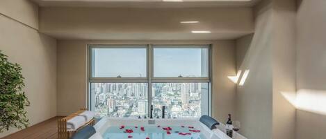 A modern spa room with a large bathtub, a city view, and a small table with a bottle and glasses.