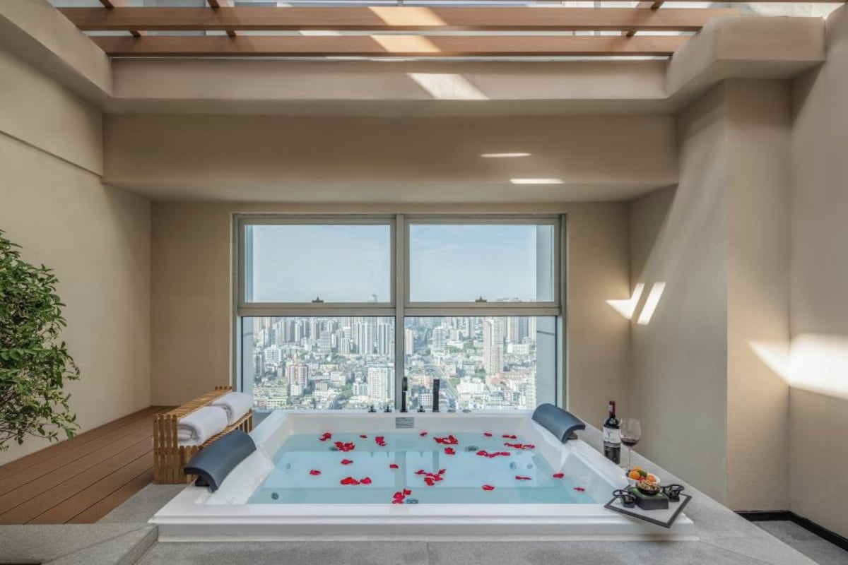Un spa moderno con una bañera grande, vistas a la ciudad y una pequeña mesa con una botella y vasos.