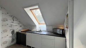 Une cuisine compacte dotée d’un puits de lumière, de meubles blancs, d’un four à micro-ondes et d’un évier.