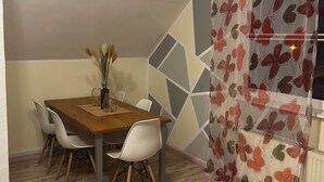 Un coin repas avec une table en bois, des chaises blanches et un vase contenant des plantes séchées.