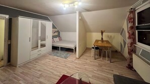 Une pièce de taille modeste comprenant un lit, une armoire, une petite table et une fenêtre avec des rideaux.