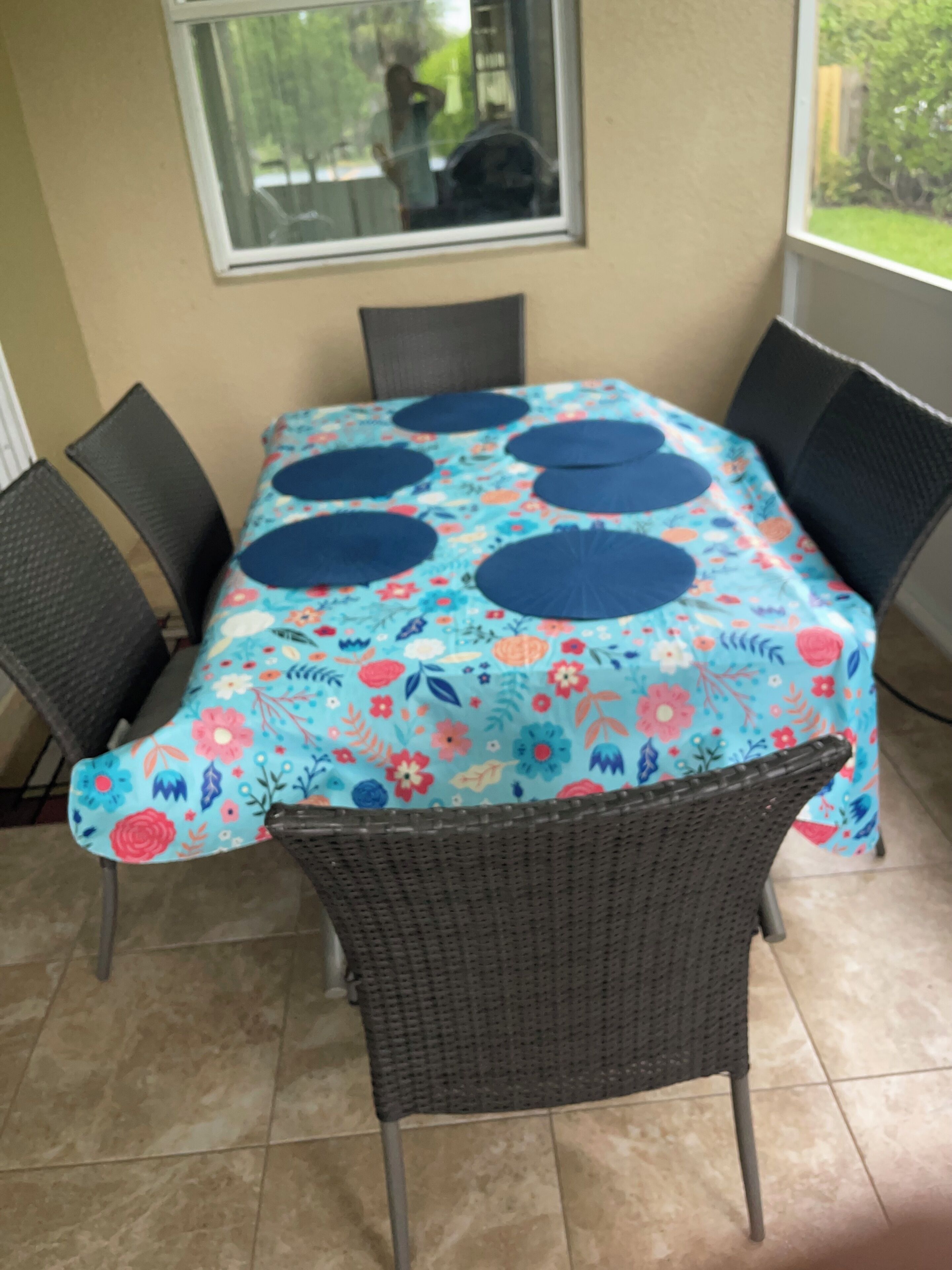 A dining table with a floral tablecloth, surrounded by wicker chairs.