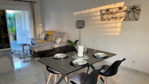 Ein Essbereich mit einem Tisch für vier Personen, einer Couch mit gemusterten Kissen und einer an der Wand befestigten Pflanze.