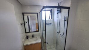 A bathroom with a glass-enclosed shower, a sink, and a mirror.