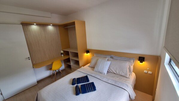 Un dormitorio con cama, mesitas de noche, escritorio y silla.