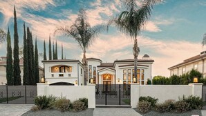 Una casa grande y moderna con fachada blanca, varias chimeneas y entrada protegida por un portón.