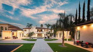 Una casa grande y moderna con un patio central, rodeada de palmeras y cipreses altos.