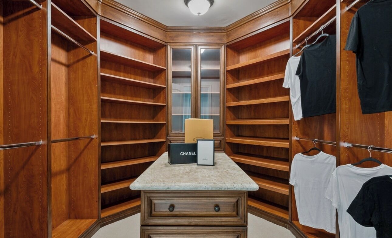 A walk-in closet with wooden shelving, a vanity with a mirror, and hanging clothes.