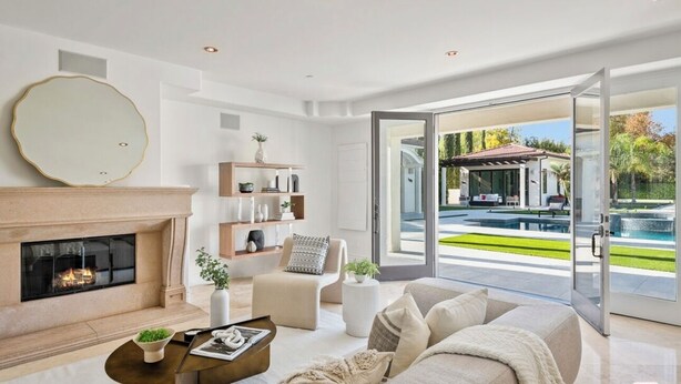 Una sala de estar moderna con chimenea, asientos cómodos, una mesa de centro y un ventanal con vistas a una piscina y zona exterior.