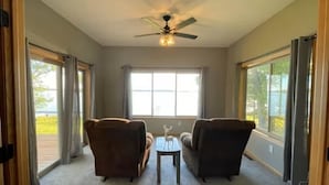 A room with two armchairs, a small table, a ceiling fan, and large windows with curtains.