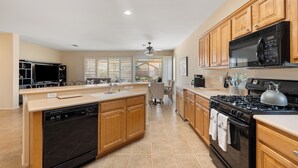 A modern kitchen with a dishwasher, stove, microwave, and wooden cabinets. -  Sun City, Palm Desert, CA, Home in 55+ Community (Palm Desert)
