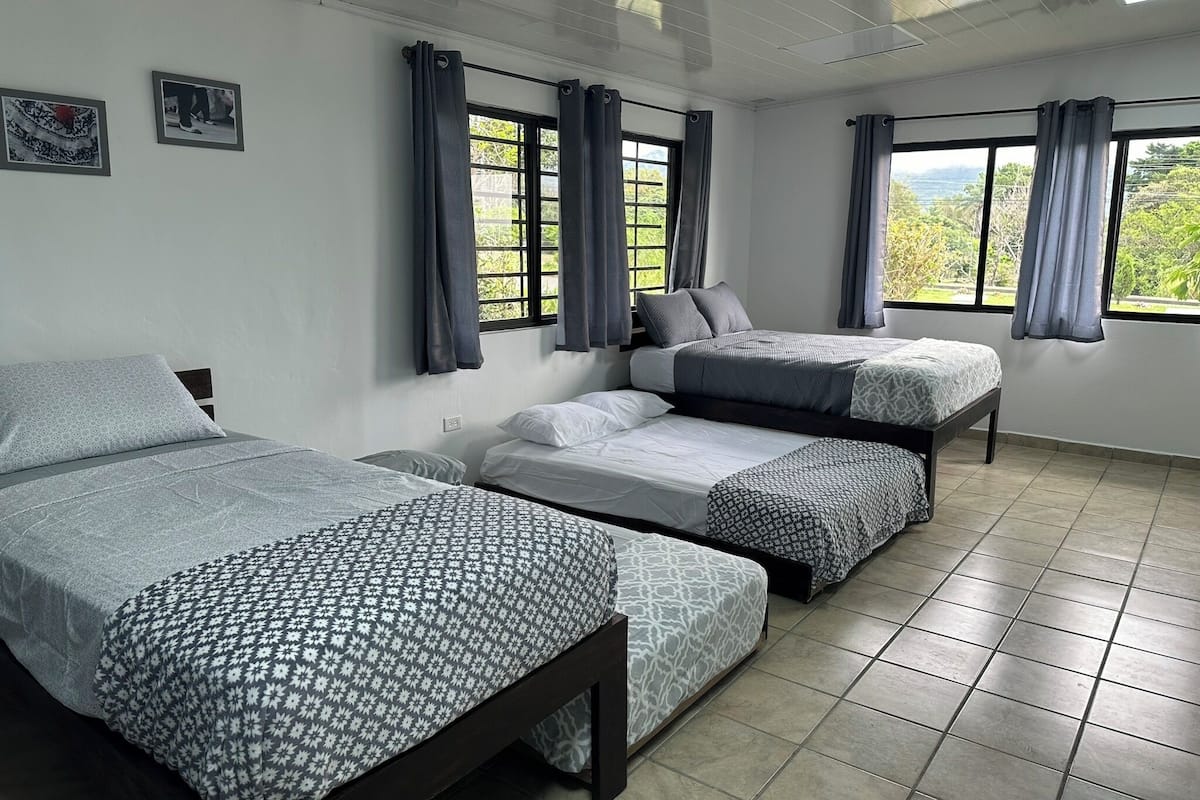 A room with three beds arranged in a row, a window with curtains, and a tiled floor.