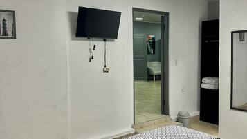 Een slaapkamer met een bed, een flatscreen televisie aan de muur, een deur naar een badkamer en een kleine prullenbak.