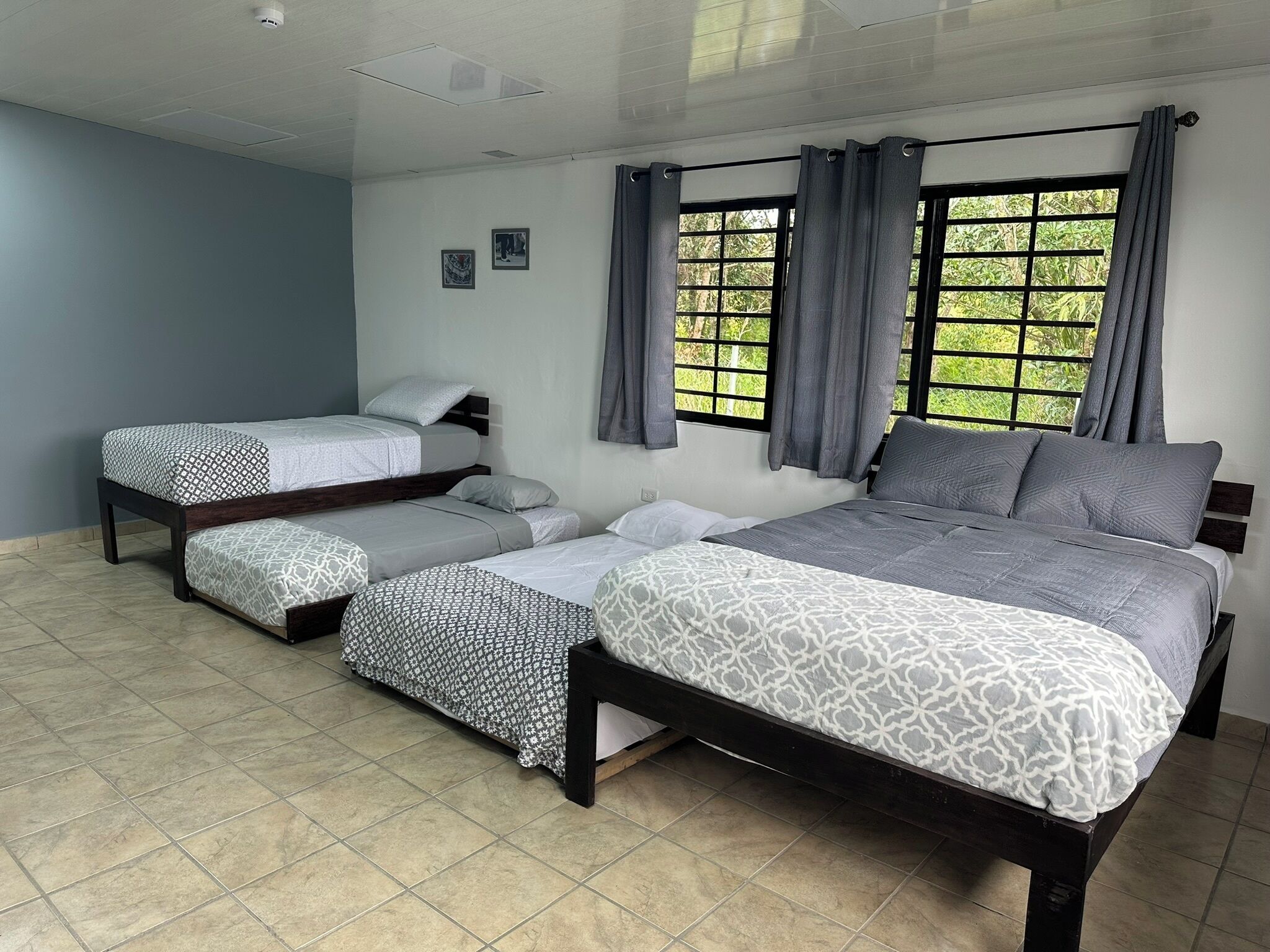 Una habitación con tres camas, una ventana con cortinas y piso de baldosas.