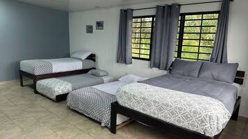 Una habitación con tres camas, una ventana con cortinas y piso de baldosas.