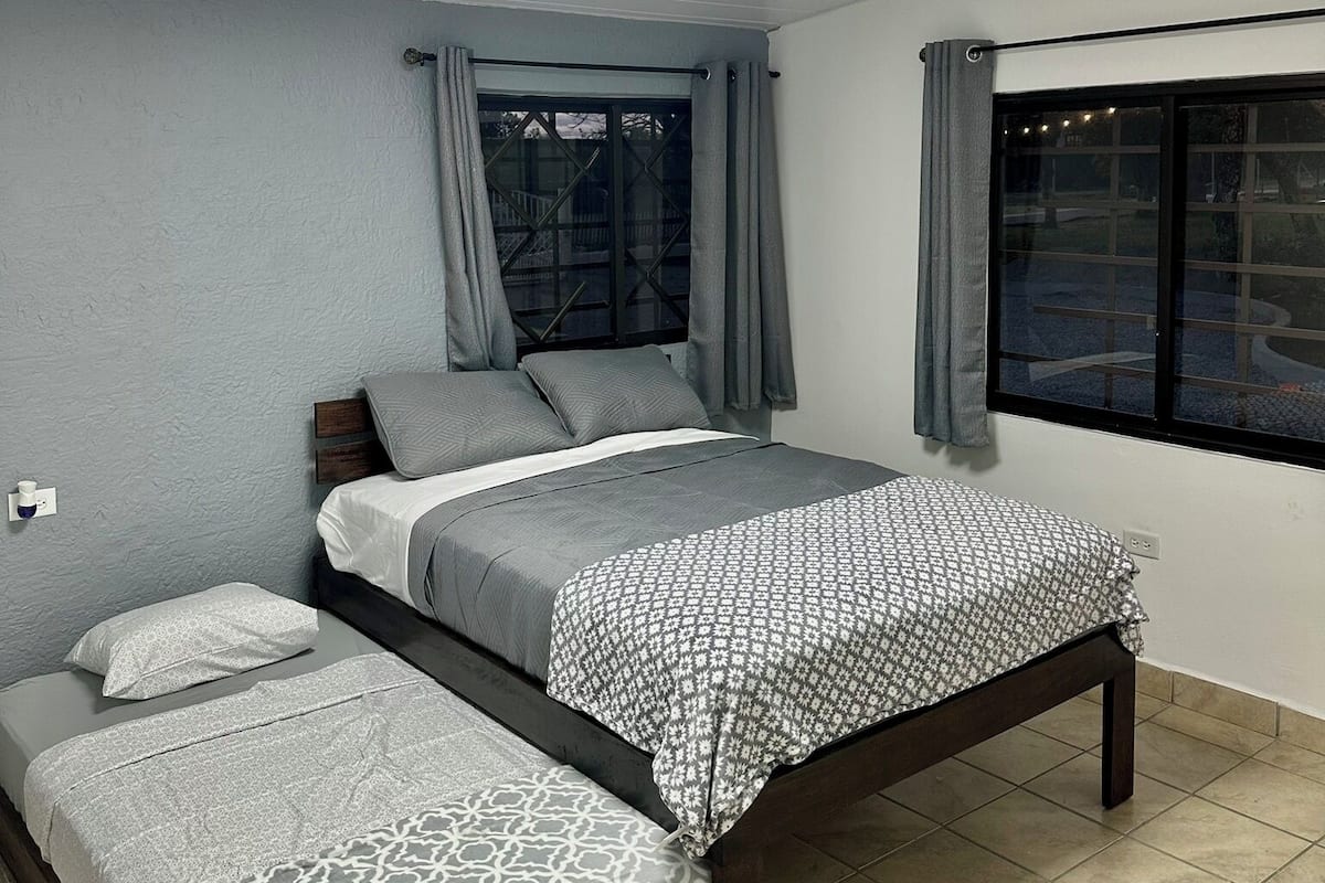 A bedroom with a bed, a bedside table, a window, and a ceiling light.