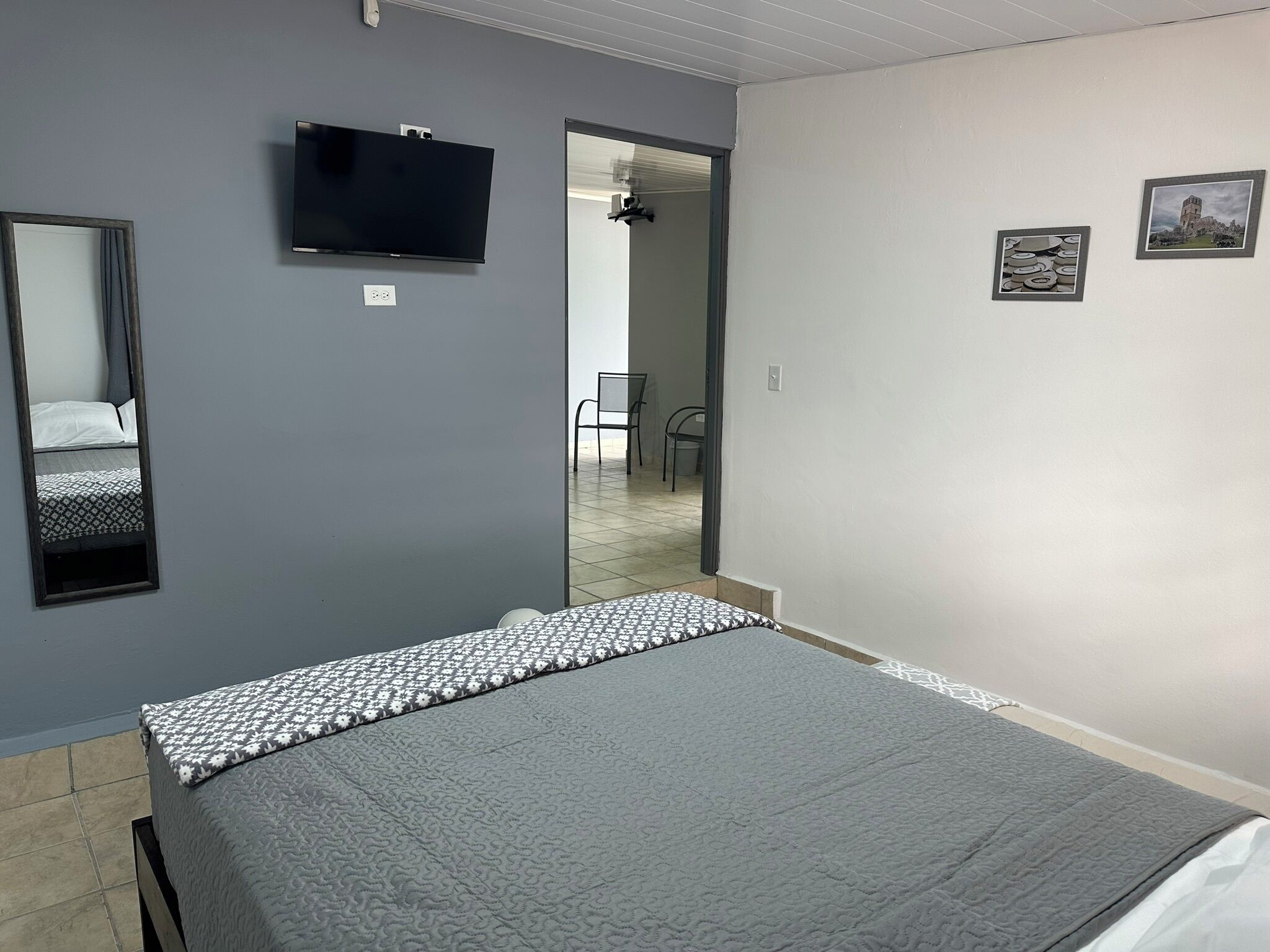 Una camera da letto con un letto, una TV a muro, uno specchio e due quadri incorniciati.