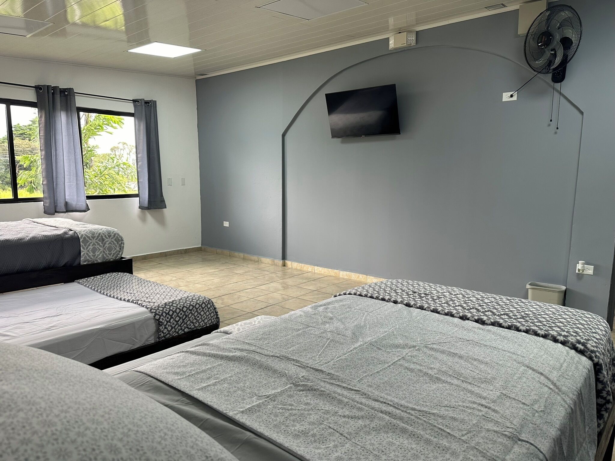 Habitación de hotel con dos camas individuales, un televisor de pantalla plana montado en la pared y un ventilador de techo.