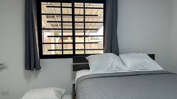 Una camera da letto con un letto, una finestra che offre vista su edifici e una presa di corrente.