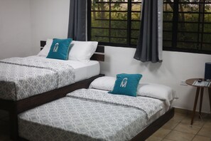 Habitación de hotel con dos camas, cada una con ropa de cama estampada y almohadas color turquesa. Hay una mesita con un control remoto y un enchufe.