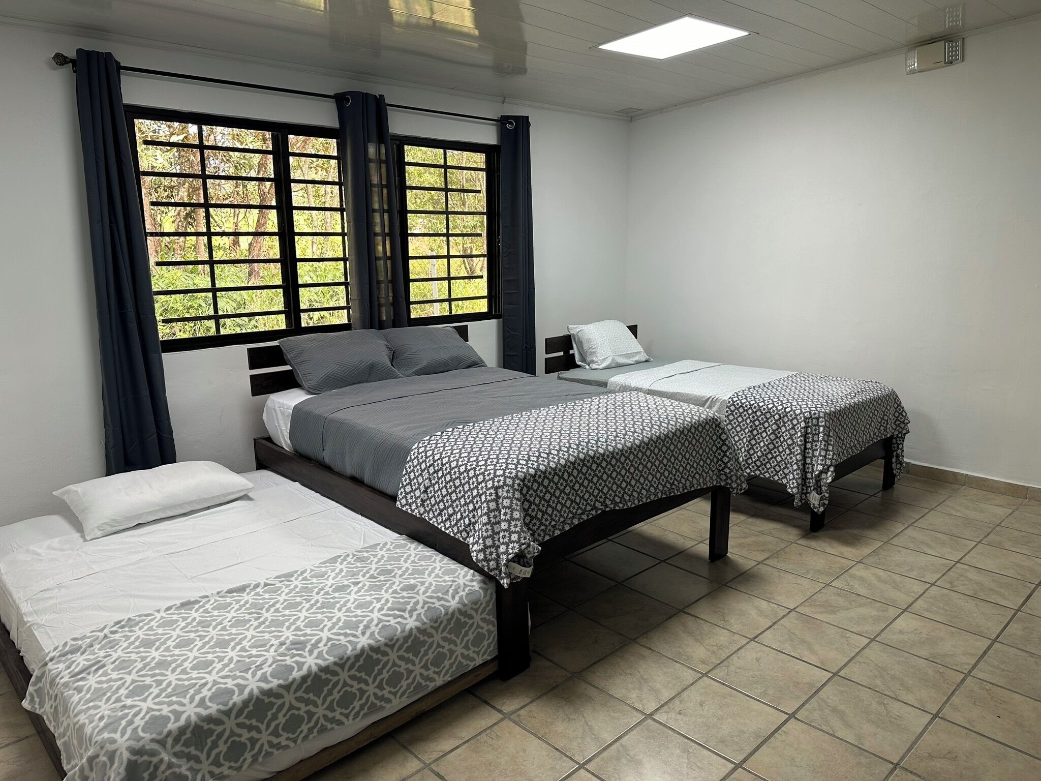 Een hotelkamer met twee enkele bedden, een groot raam met gordijnen en een betegelde vloer.