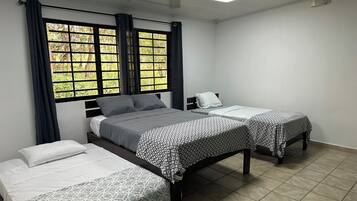 Een hotelkamer met twee enkele bedden, een groot raam met gordijnen en een betegelde vloer.