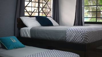 A single bed with a patterned bedspread and pillows, a small bedside table, and a window with a lattice design.