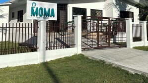 Un edificio blanco con un letrero que dice "MOMA GUEST HOUSE" y una entrada con portón.