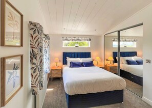 A bedroom with a bed, two bedside tables, a mirror, a window, and a door. - 1 bedroom accommodation in Chipping (Chipping)