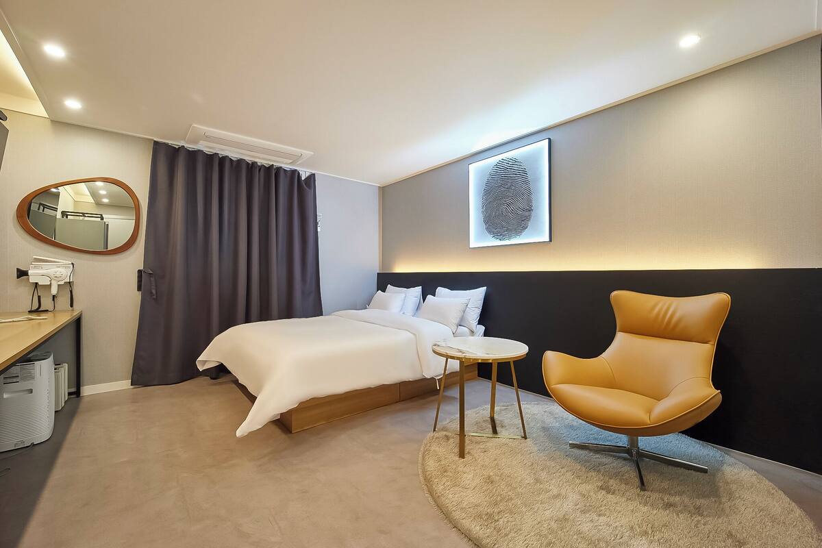 A modern hotel room with a bed, a round table, a chair, a mirror, and a wall-mounted fingerprint scanner.