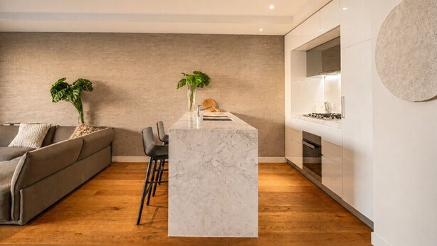 Una cucina moderna con isola in marmo, pavimento in legno e divano grigio nella zona soggiorno.