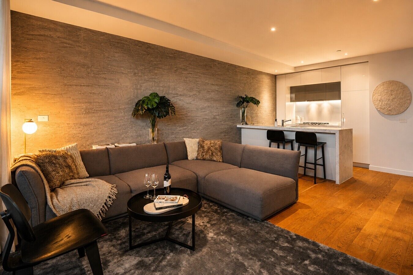 A modern living room with a sectional sofa, a coffee table, and a small kitchen area in the background.