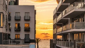 Un edificio moderno con balconi affacciato su uno specchio d'acqua al tramonto.