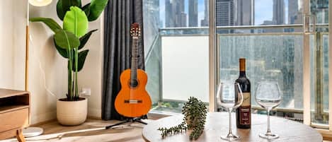 Ein modernes Zimmer mit Stadtblick, einer Gitarre, einem Tisch mit Weingläsern und einer Topfpflanze.