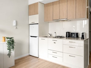 A modern kitchen with white cabinets, a stainless steel refrigerator, a coffee maker, and a plant on the counter.