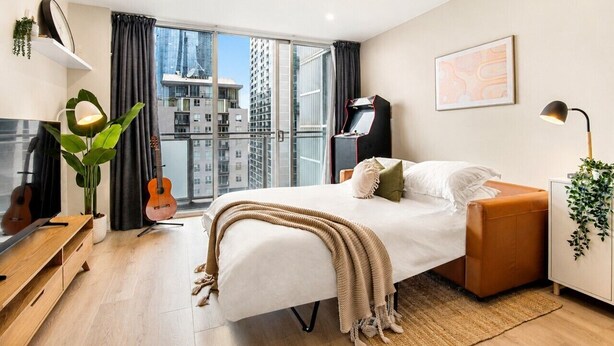 Een moderne slaapkamer met een bed, een gitaar, een televisie en uitzicht over de stad.