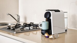Een keuken met een gasfornuis, een koffieapparaat en een glas water op het aanrecht.