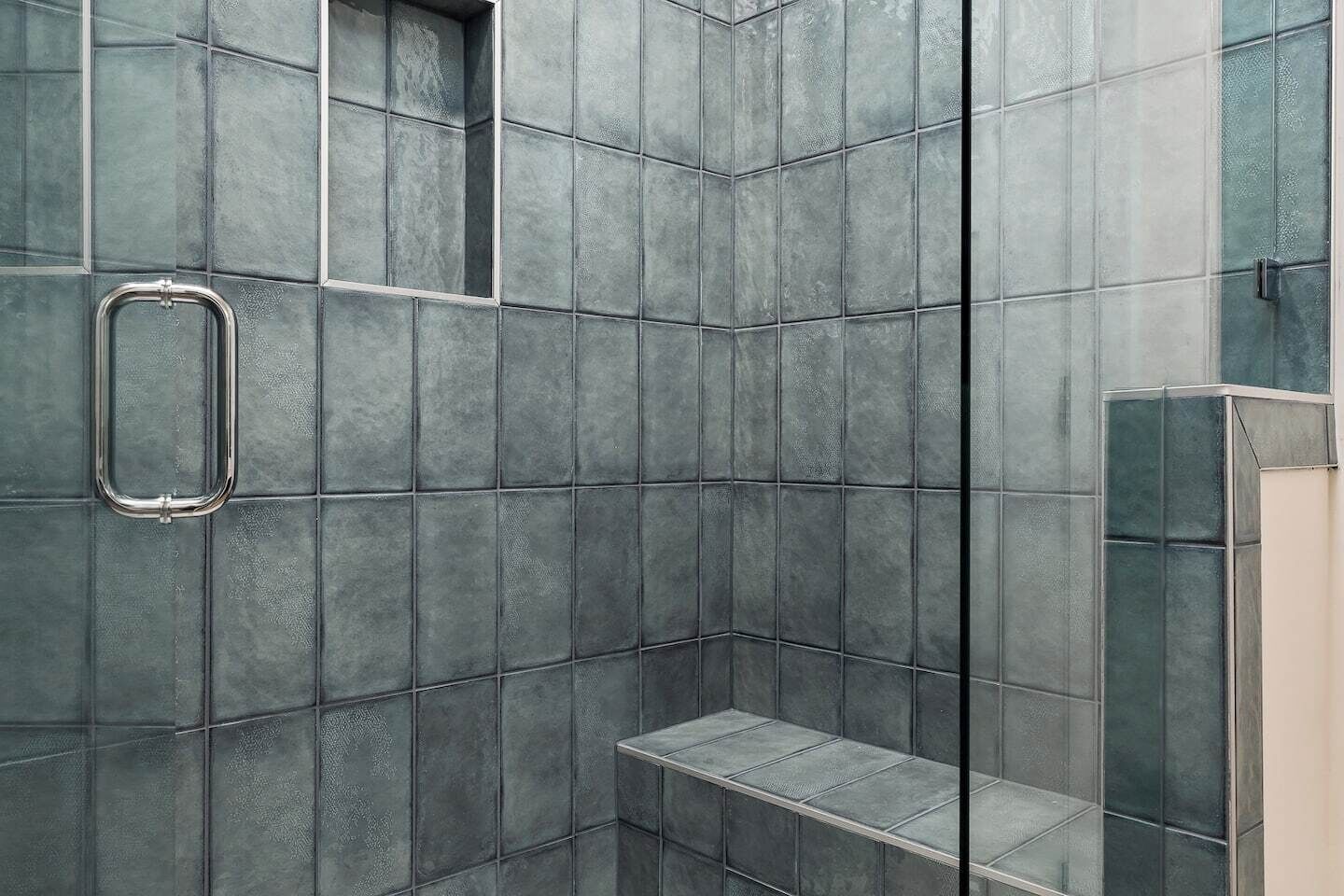 A shower area with a glass enclosure, a metal grab bar, and a bench.
