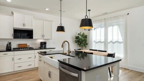 Une cuisine moderne avec des meubles blancs, un îlot central, un plan de travail noir et des luminaires suspendus.