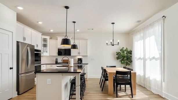 Une cuisine moderne dotée d’un îlot central, d’appareils électroménagers en acier inoxydable et de luminaires suspendus.
