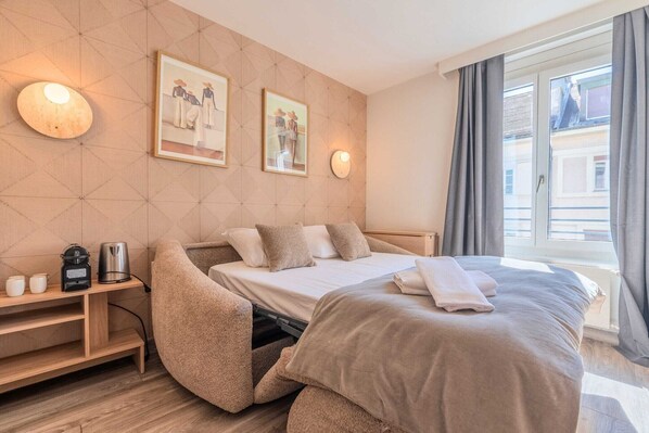 A neatly arranged bedroom with a bed, bedside table, and a small seating area.