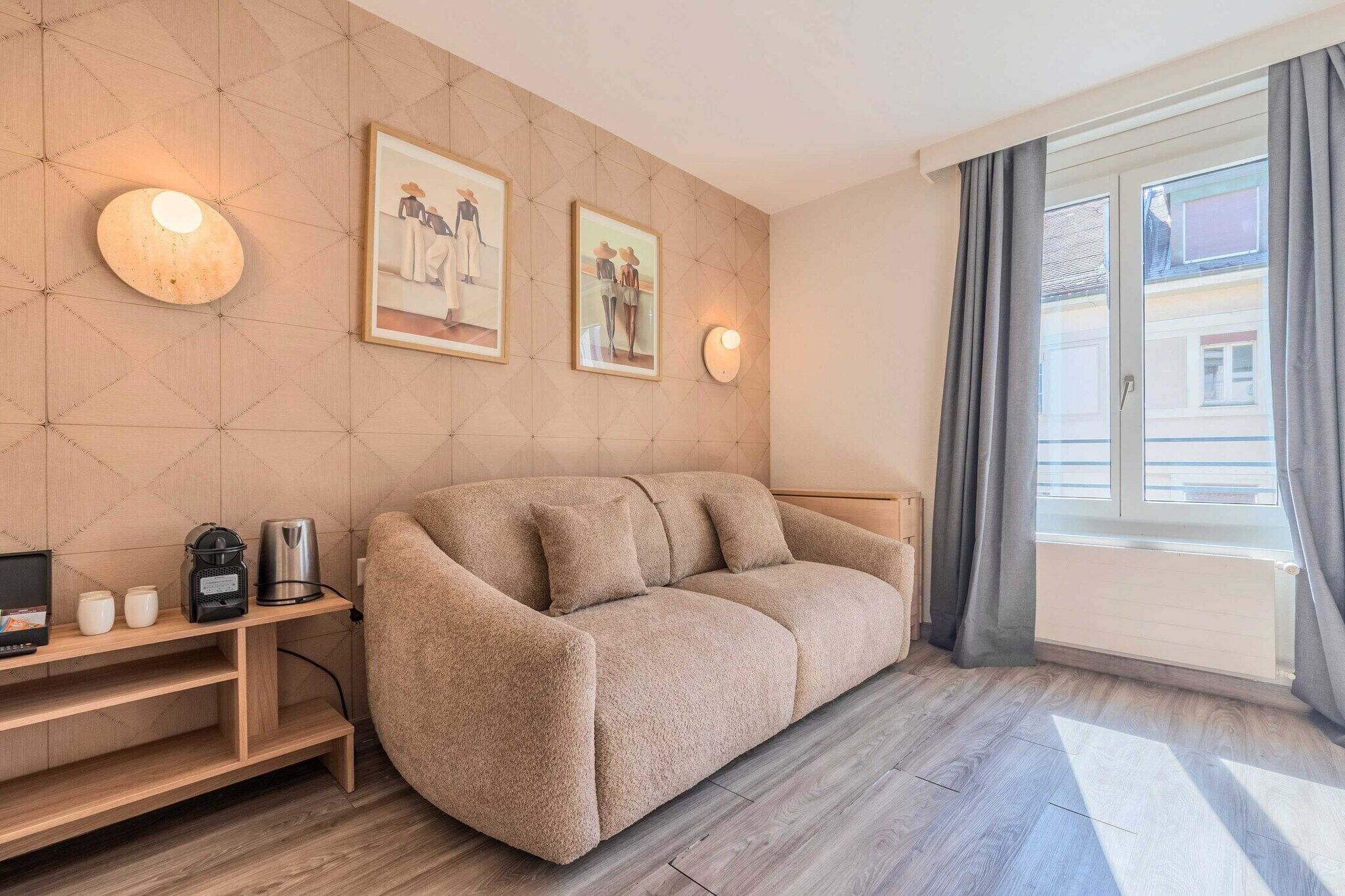 Ein modernes Wohnzimmer mit einer Couch, einem Couchtisch und einem Fernseher. Zwei Wandleuchten und gerahmte Bilder zieren die Wand.
