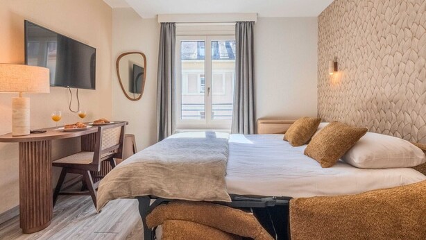 Une chambre d’hôtel avec un lit, un bureau doté d’une lampe, une chaise et un téléviseur.