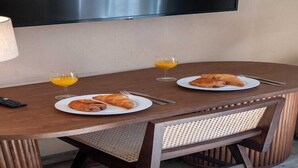 Une table à manger avec deux assiettes de croissants et deux verres de jus d’orange, une télécommande et un téléviseur fixé au mur.
