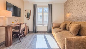 Un salon moderne avec un canapé, un téléviseur fixé au mur, une table à manger avec des chaises et une fenêtre avec des rideaux.